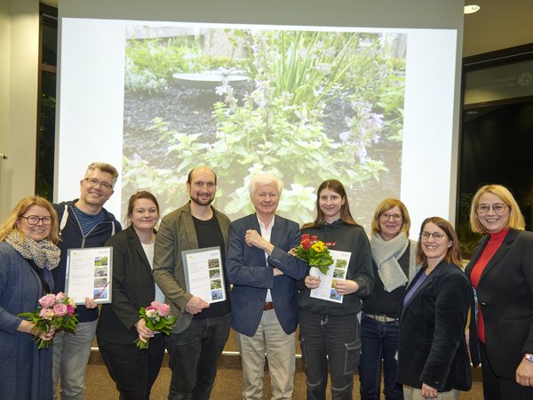 Eine Gruppe von glücklich aussehenden Menschen mit Urkunden und Blumensträußen.